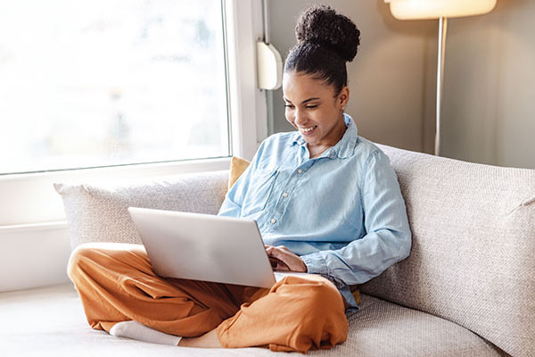 A woman sits on her living room sofa and works on her laptop computer.